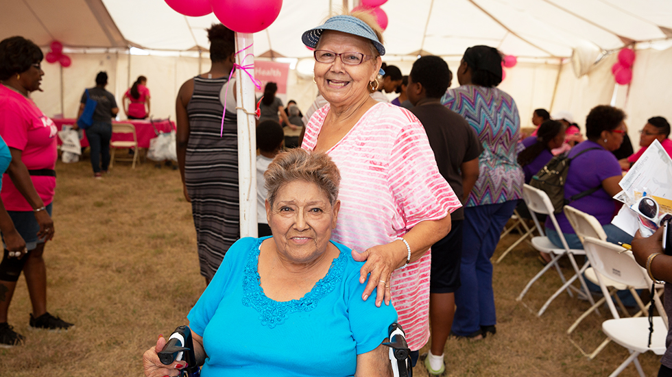 Woman in wheelchair smiling with another woman behind her smiling