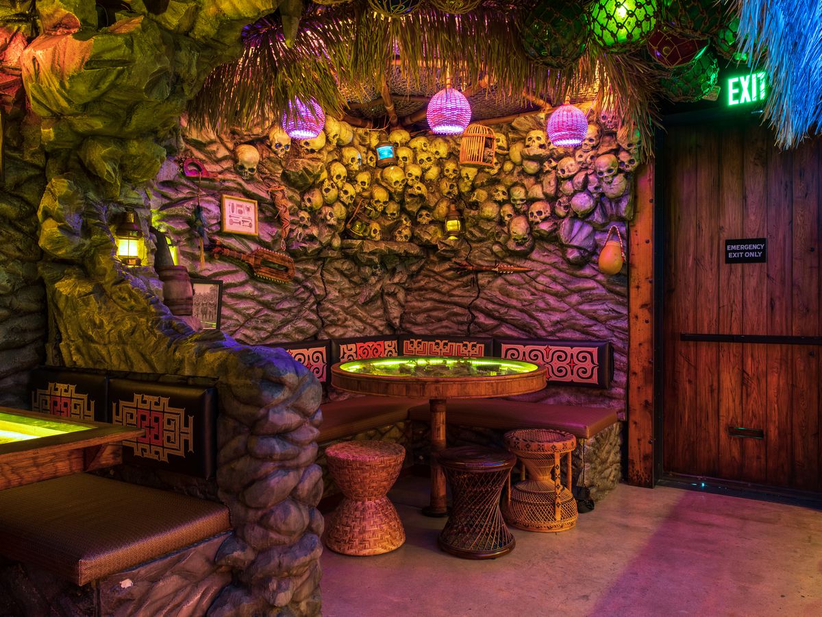 Under colorful lamps, fronds, and netting, a corner booth is nestled into a rock wall inlaid with skulls.