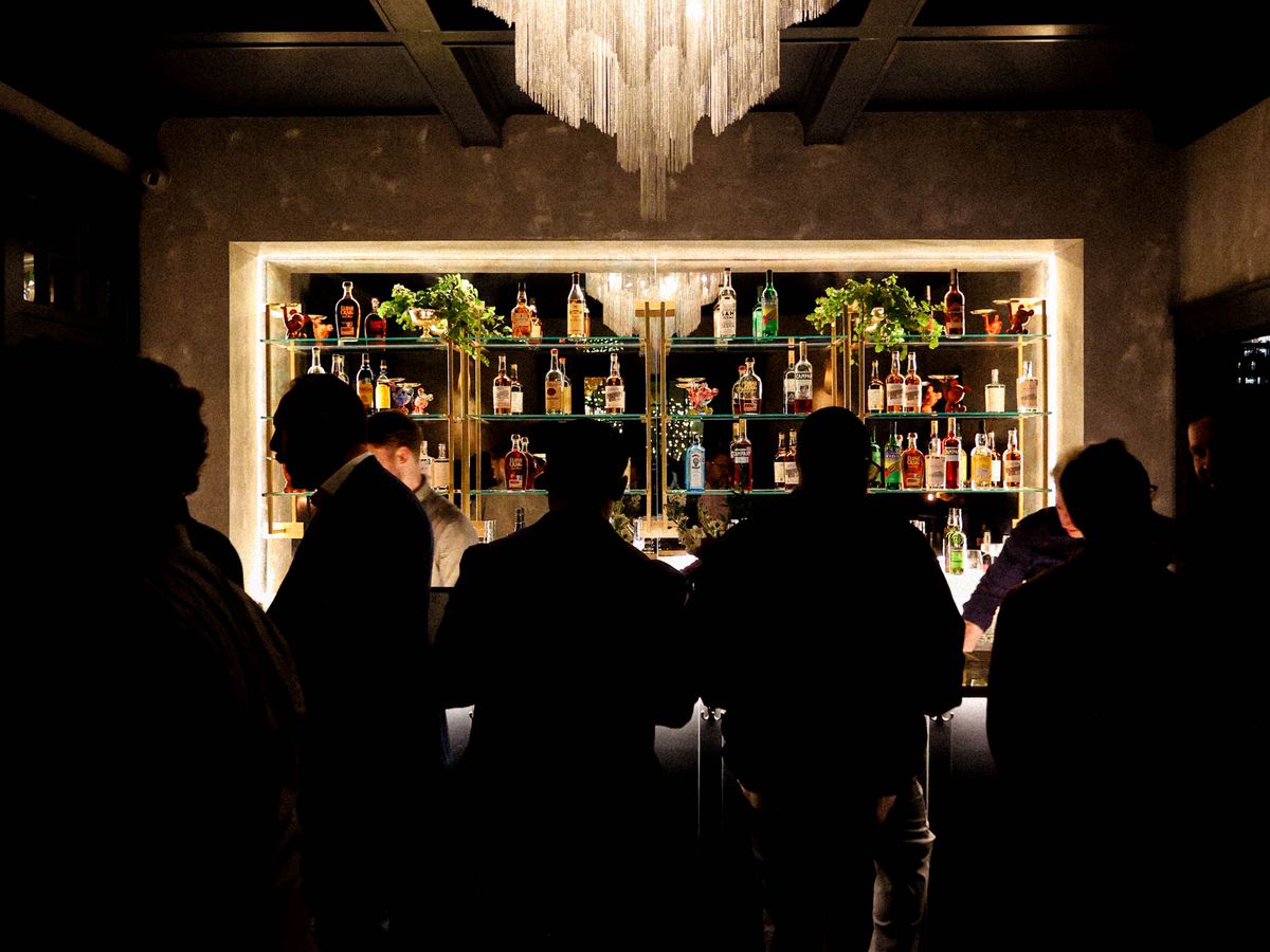 People standing in front of a bar underneath a chandelier.