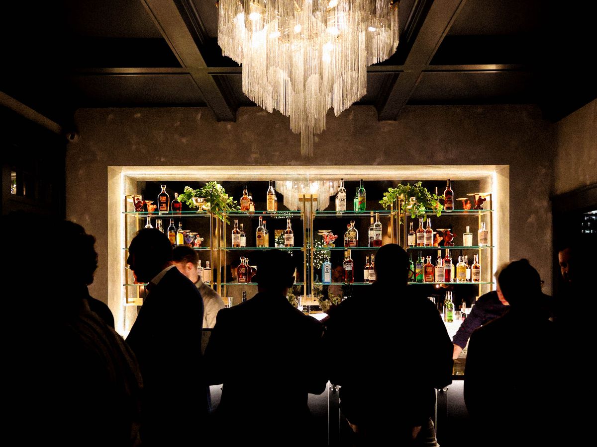 People standing in front of a bar underneath a chandelier.