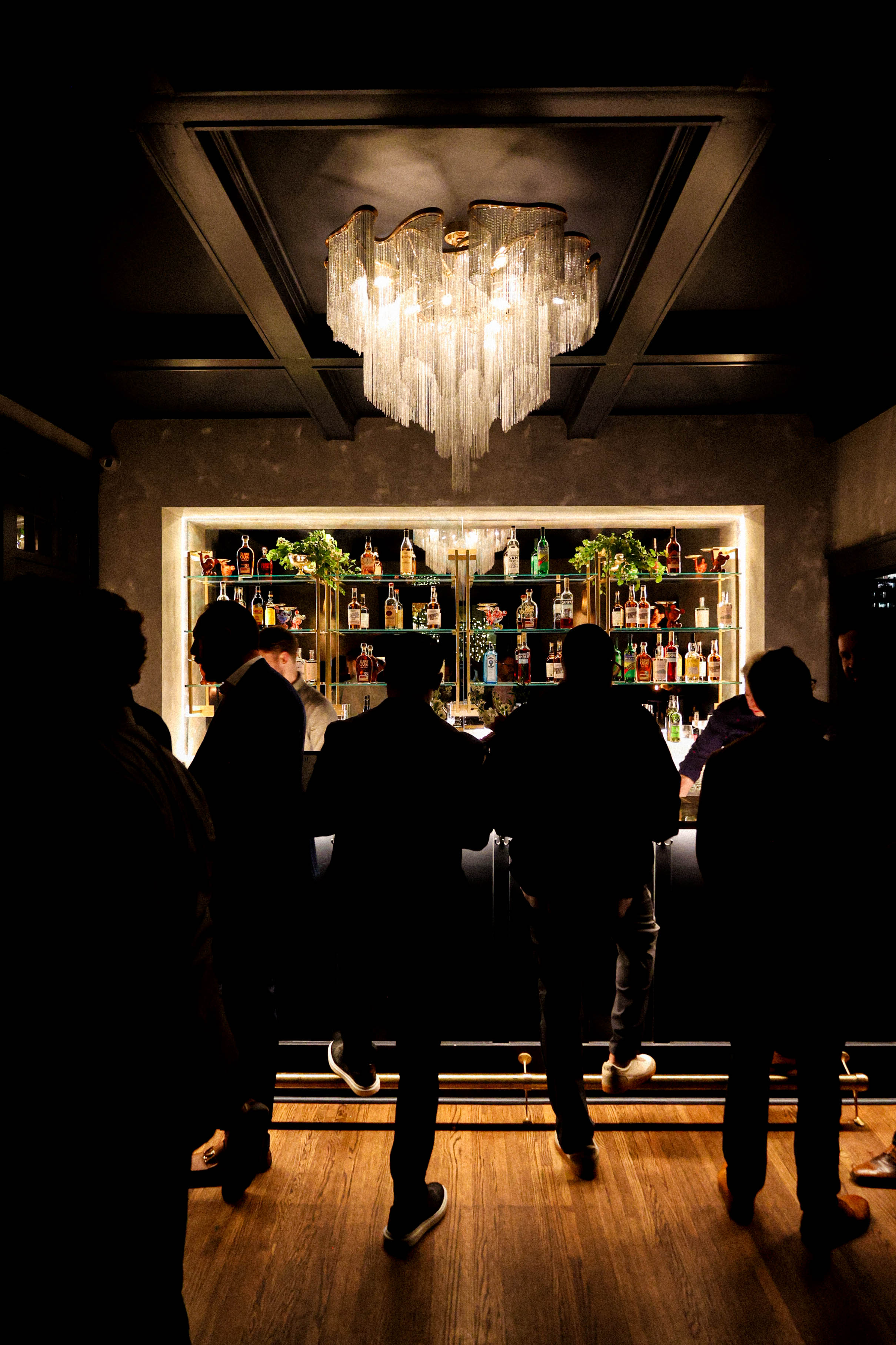 People standing in front of a bar underneath a chandelier.