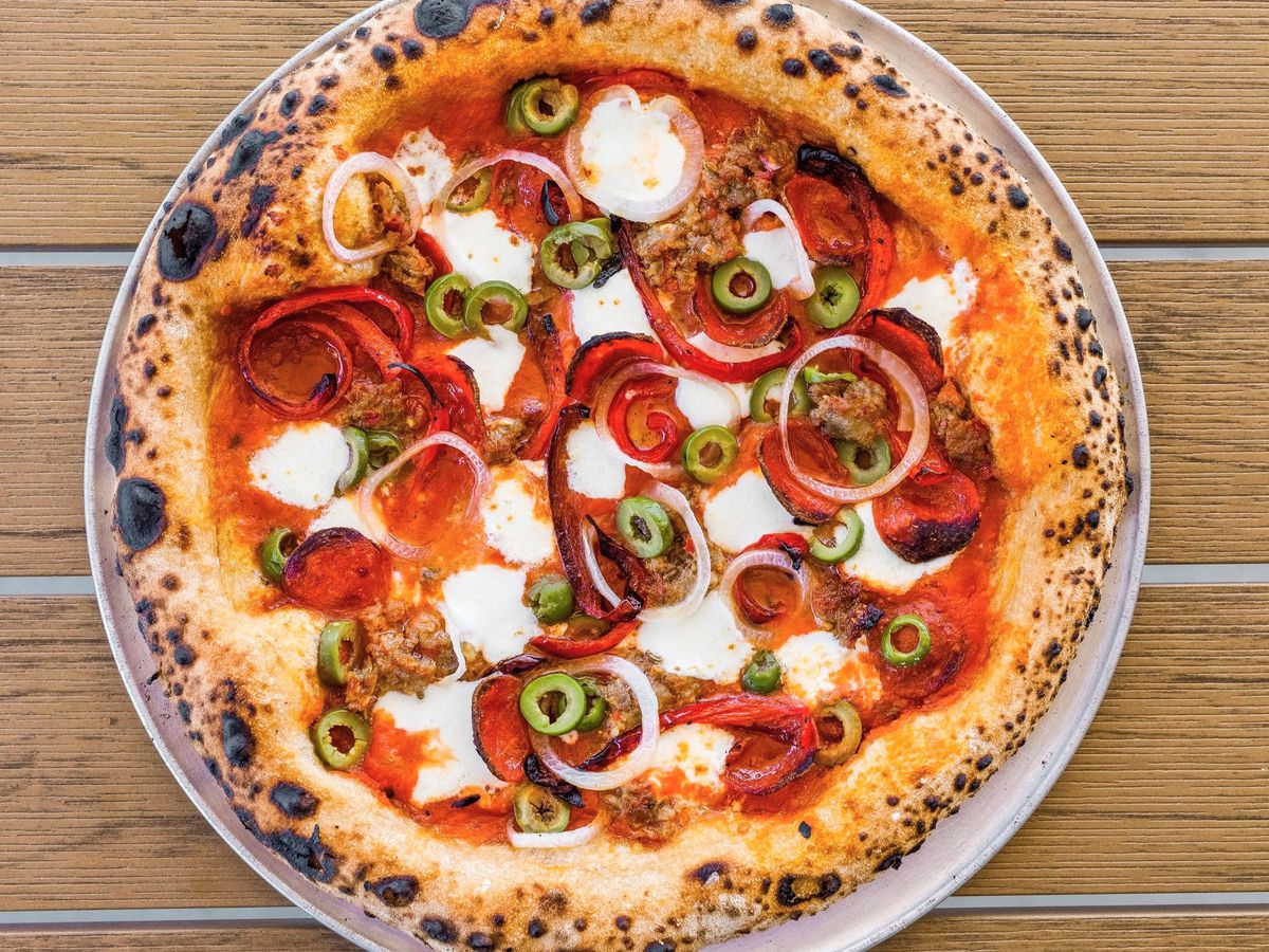 A pizza pie topped with meats, veggies, and white cheese.
