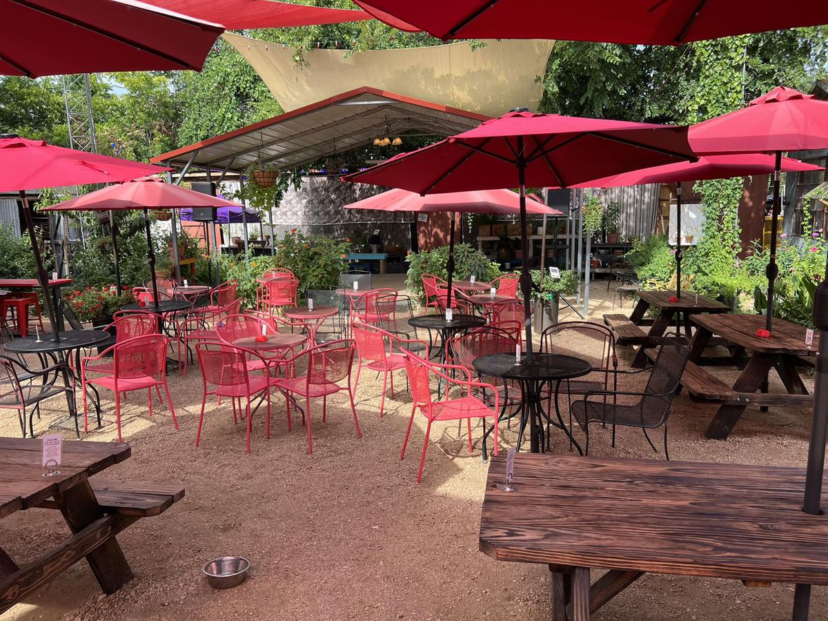 A bar patio with tables, red chairs, and red umbrellas.