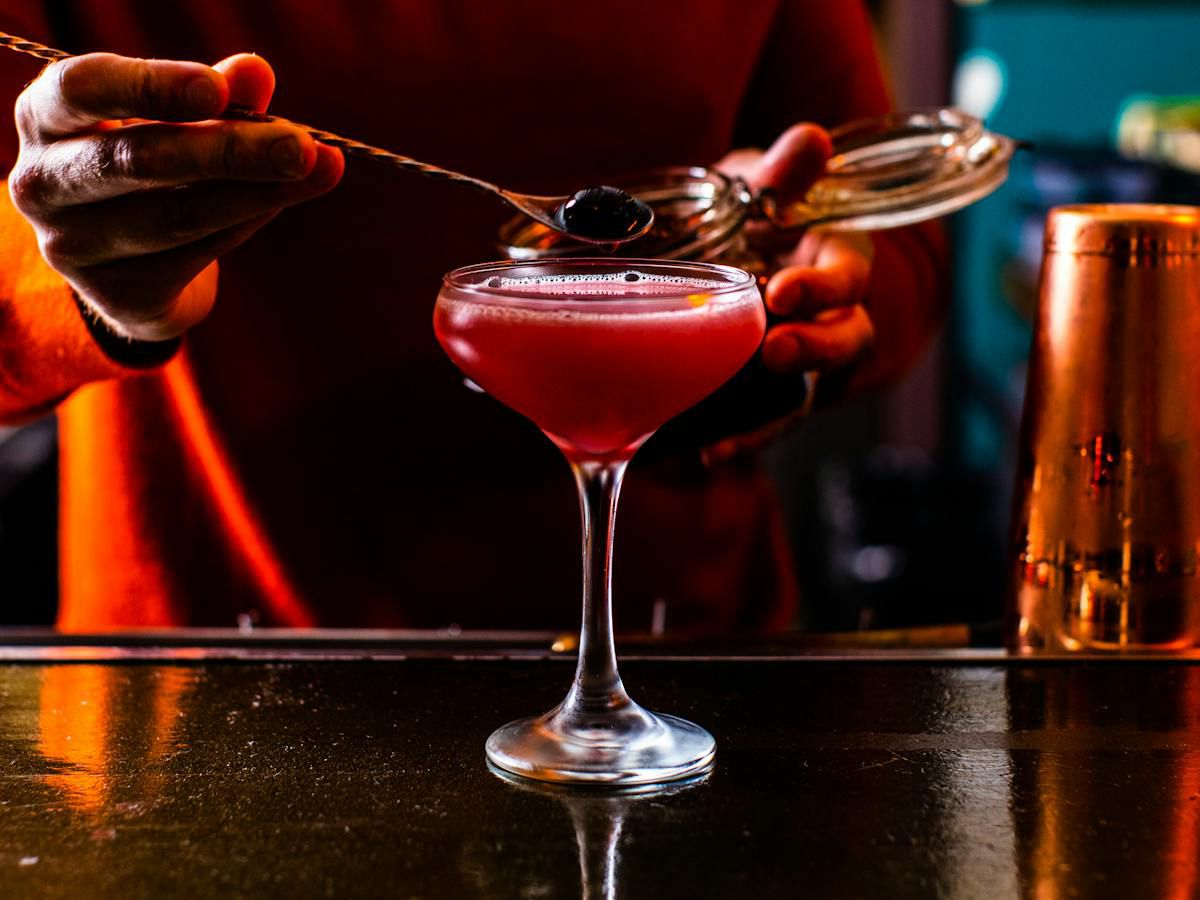 Someone adding a cherry to a pink cocktail.