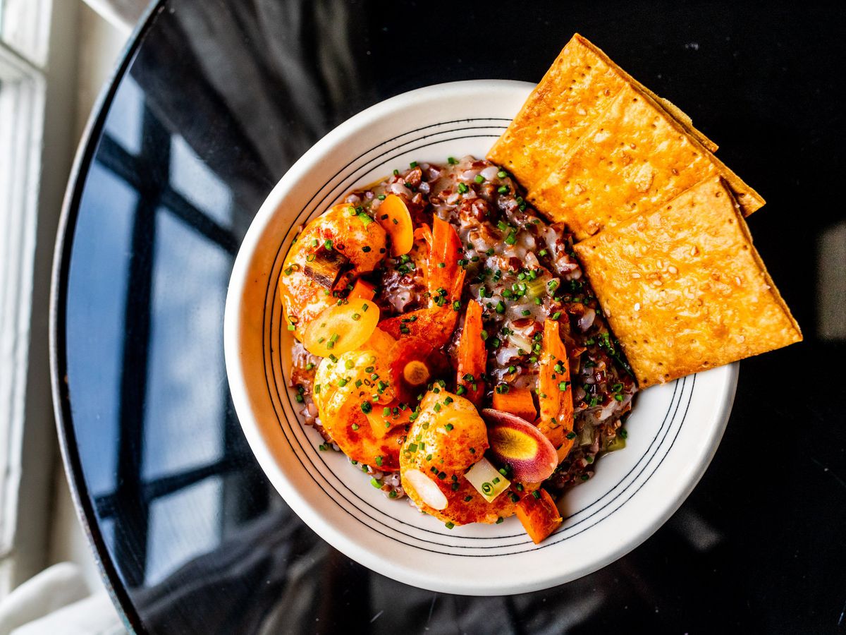 A plate of shrimp, black rice, and crackers. 
