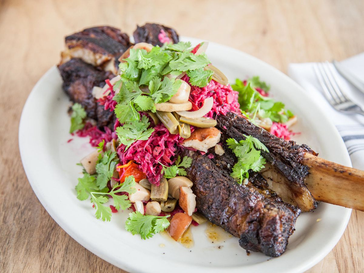 A giant piece of meat on bone on a plate with leafy greens on top of it.