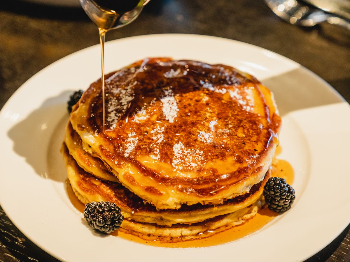 Someone pouring syrup onto a stack of pancakes.