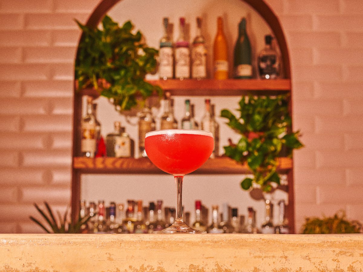 A cocktail on a bar in front of shelves of alcohol bottles.