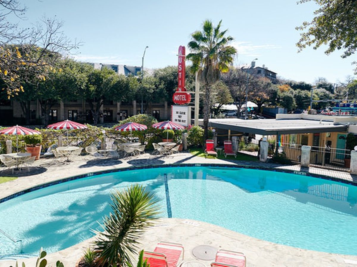 The kidney bean shaped pool at the Austin Motel, with white tables and chairs around it, each with a red and white striped umbrella.