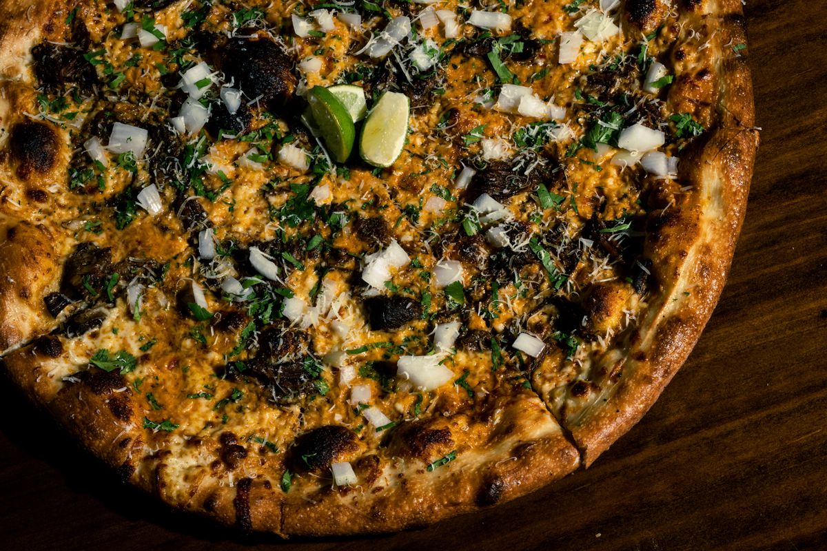 A pizza topped with onion, birria beef, cilantro, and lime.