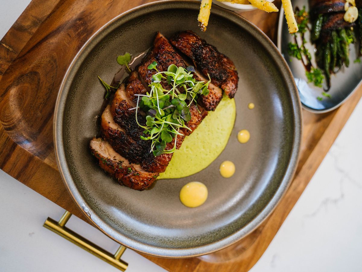 A serving tray of sliced meat with green sauce underneath it.