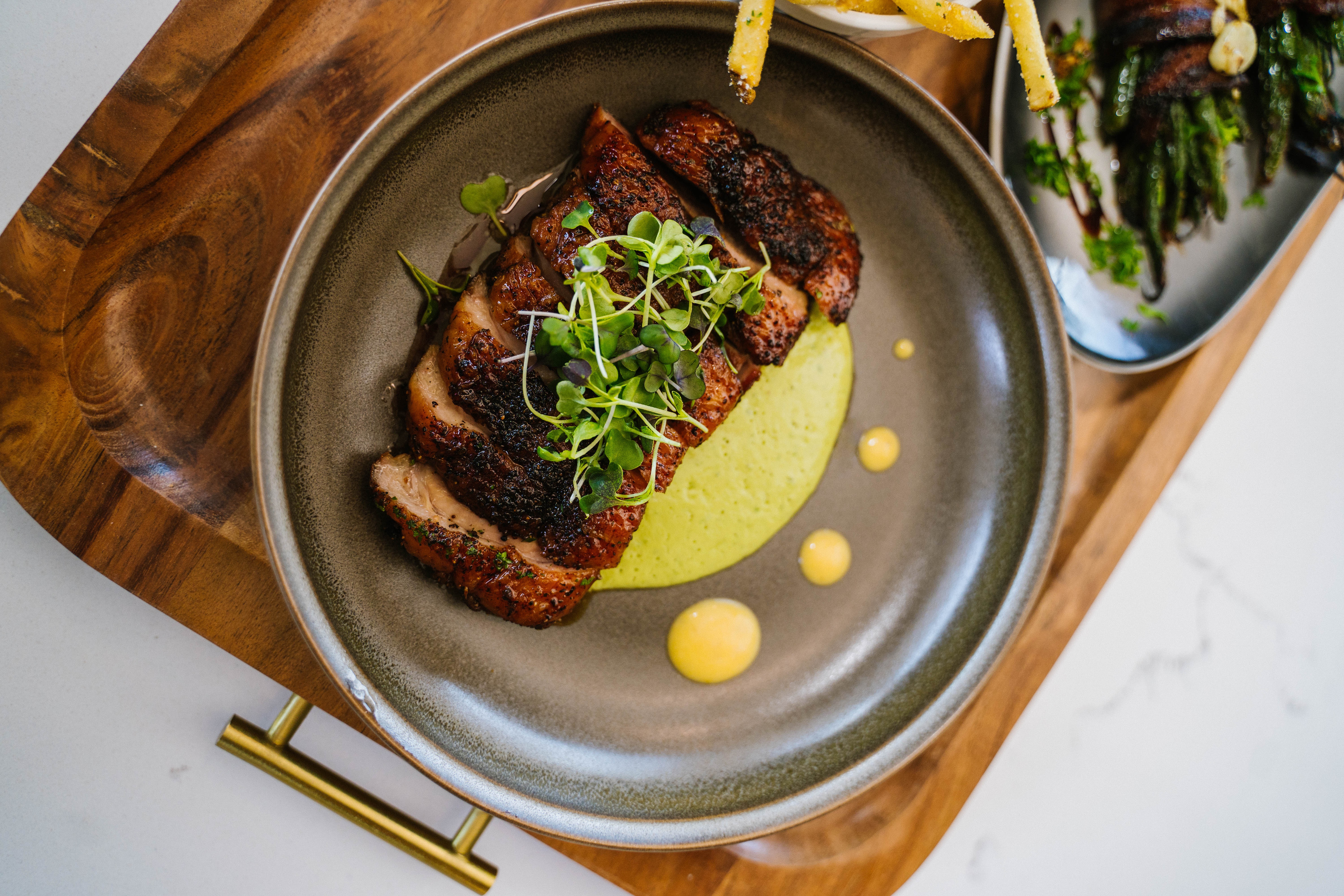 A serving tray of sliced meat with green sauce underneath it.
