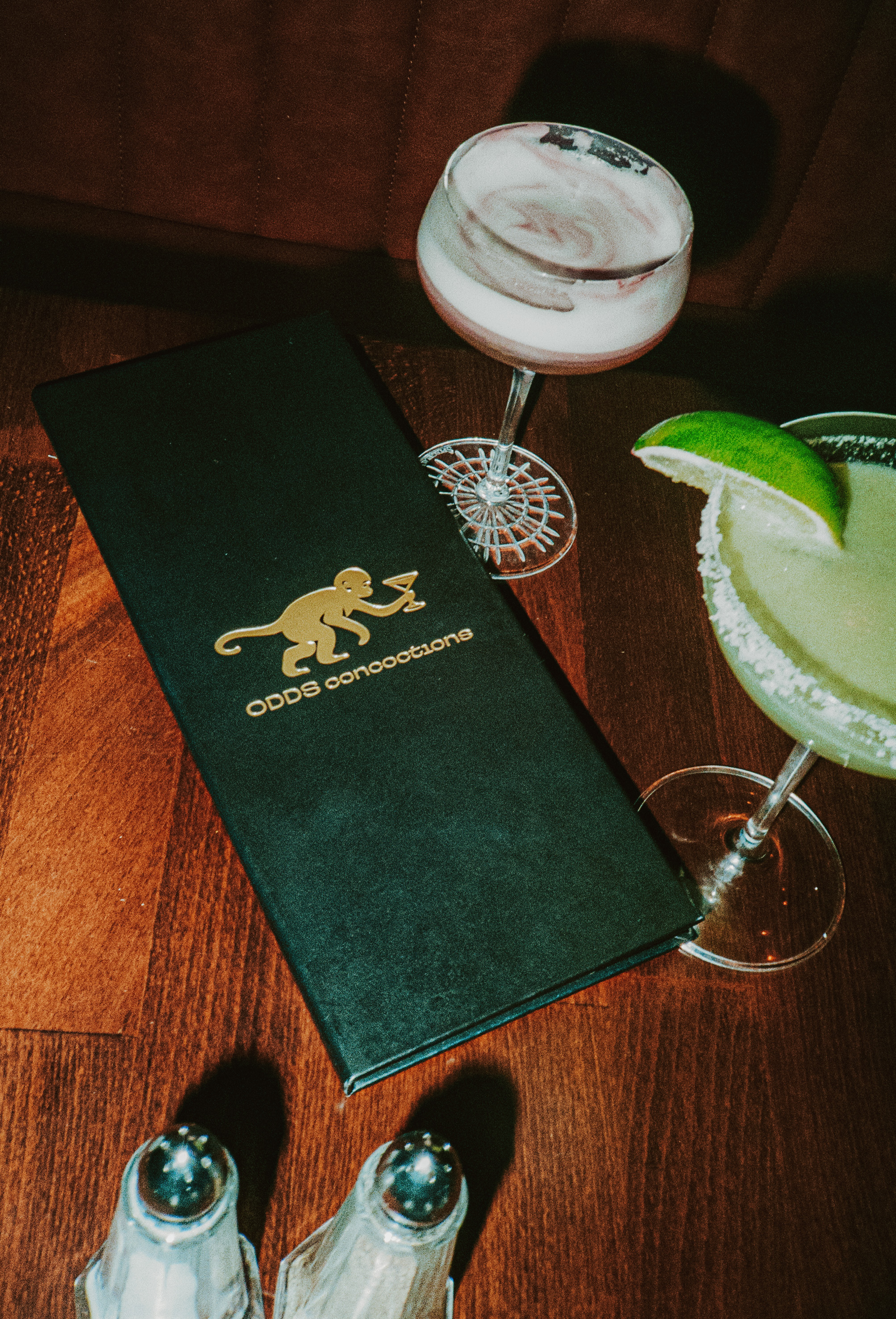 A cocktail menu in a covered jacked with gold-embossed letters that read “Odds Annotations.” To the left and top are cocktails.