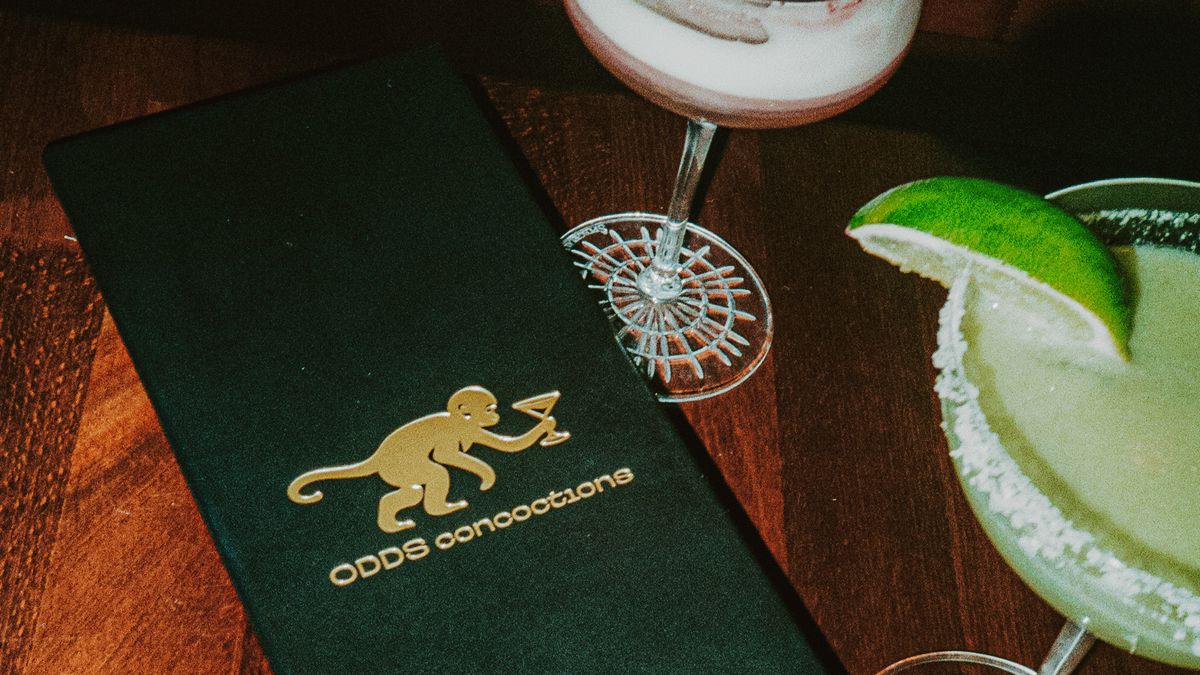 A cocktail menu in a covered jacked with gold-embossed letters that read “Odds Annotations.” To the left and top are cocktails.
