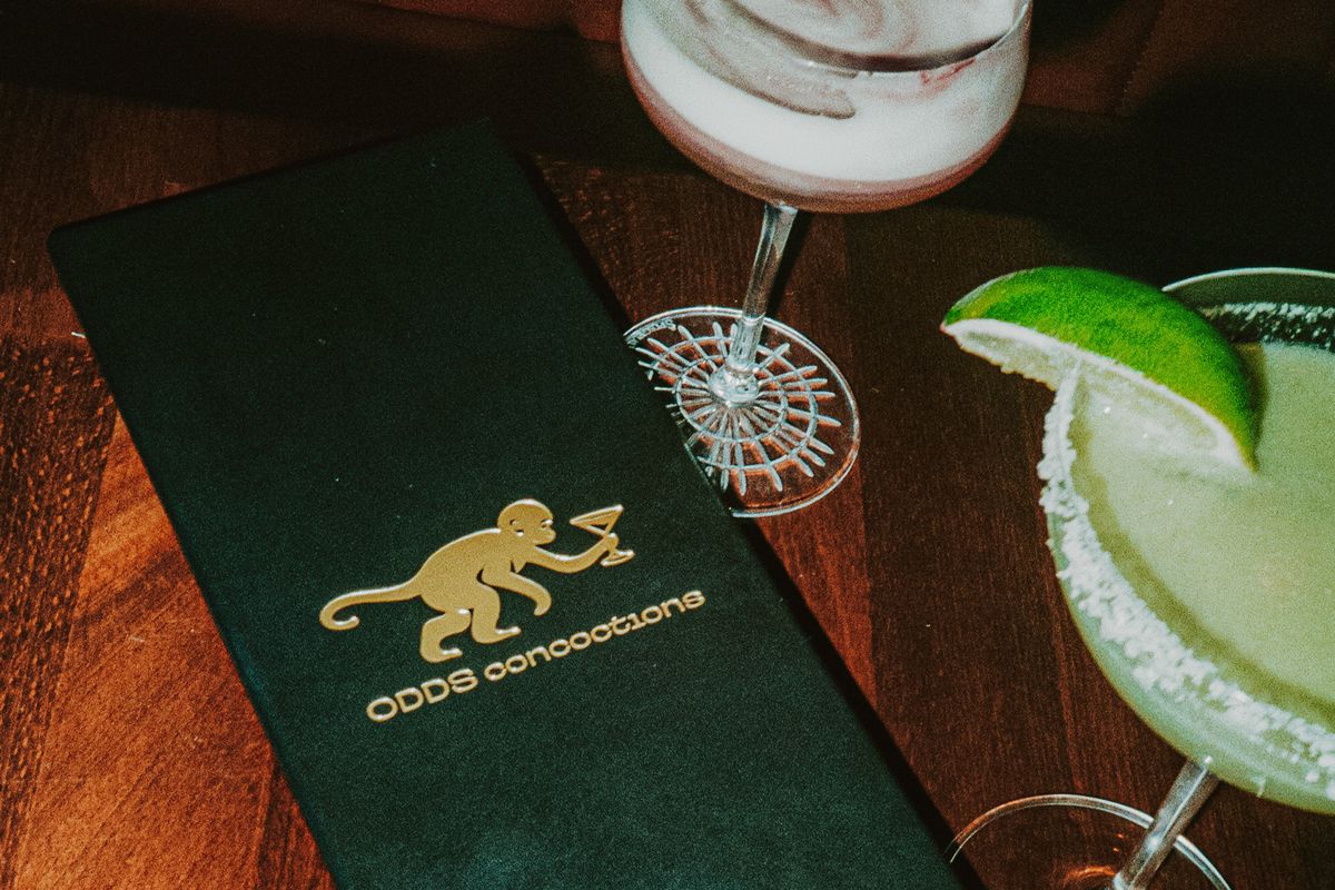 A cocktail menu in a covered jacked with gold-embossed letters that read “Odds Annotations.” To the left and top are cocktails.
