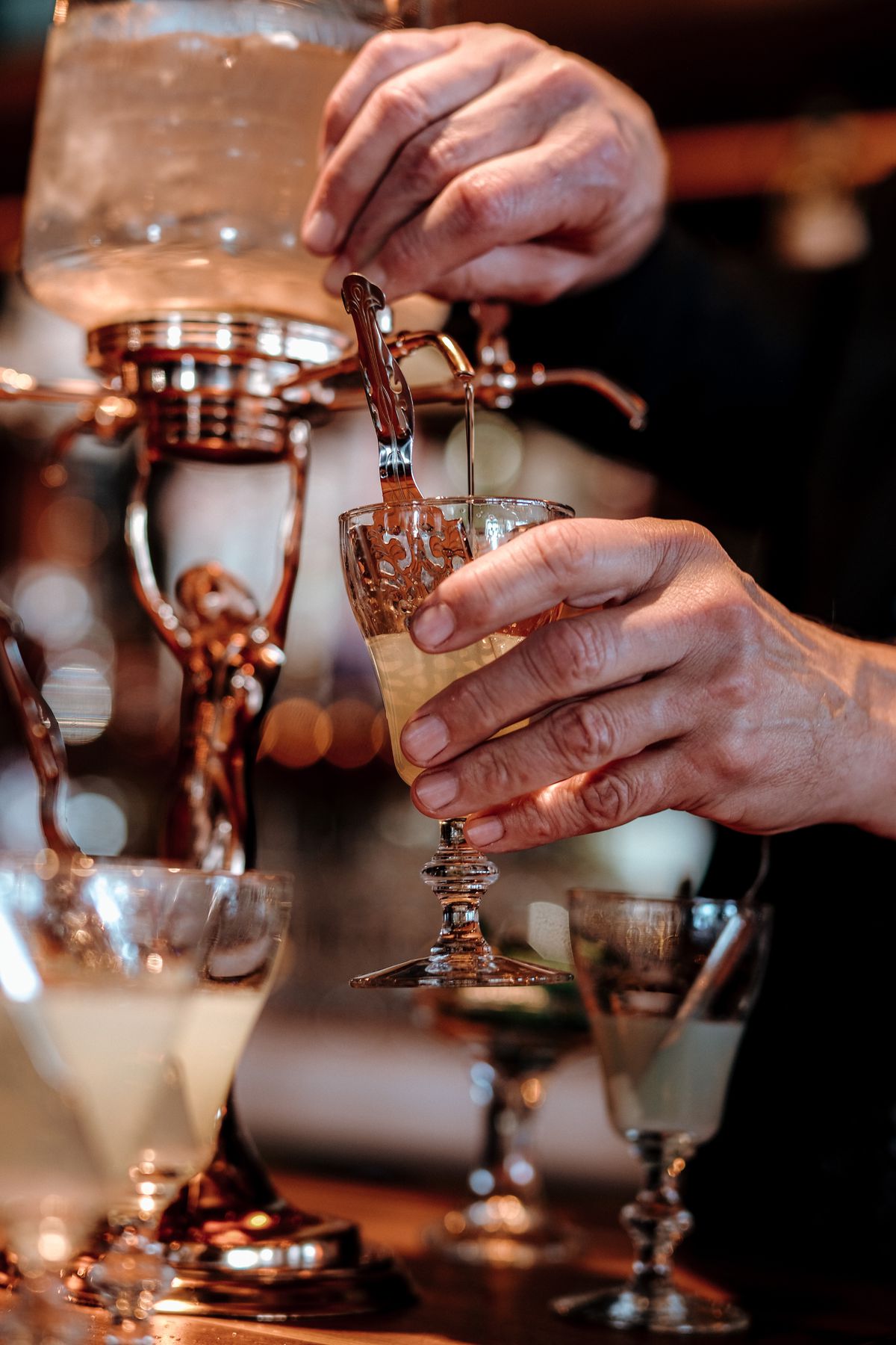 Hands push down on a dispenser with alcohol in it, pressing it into a glass.
