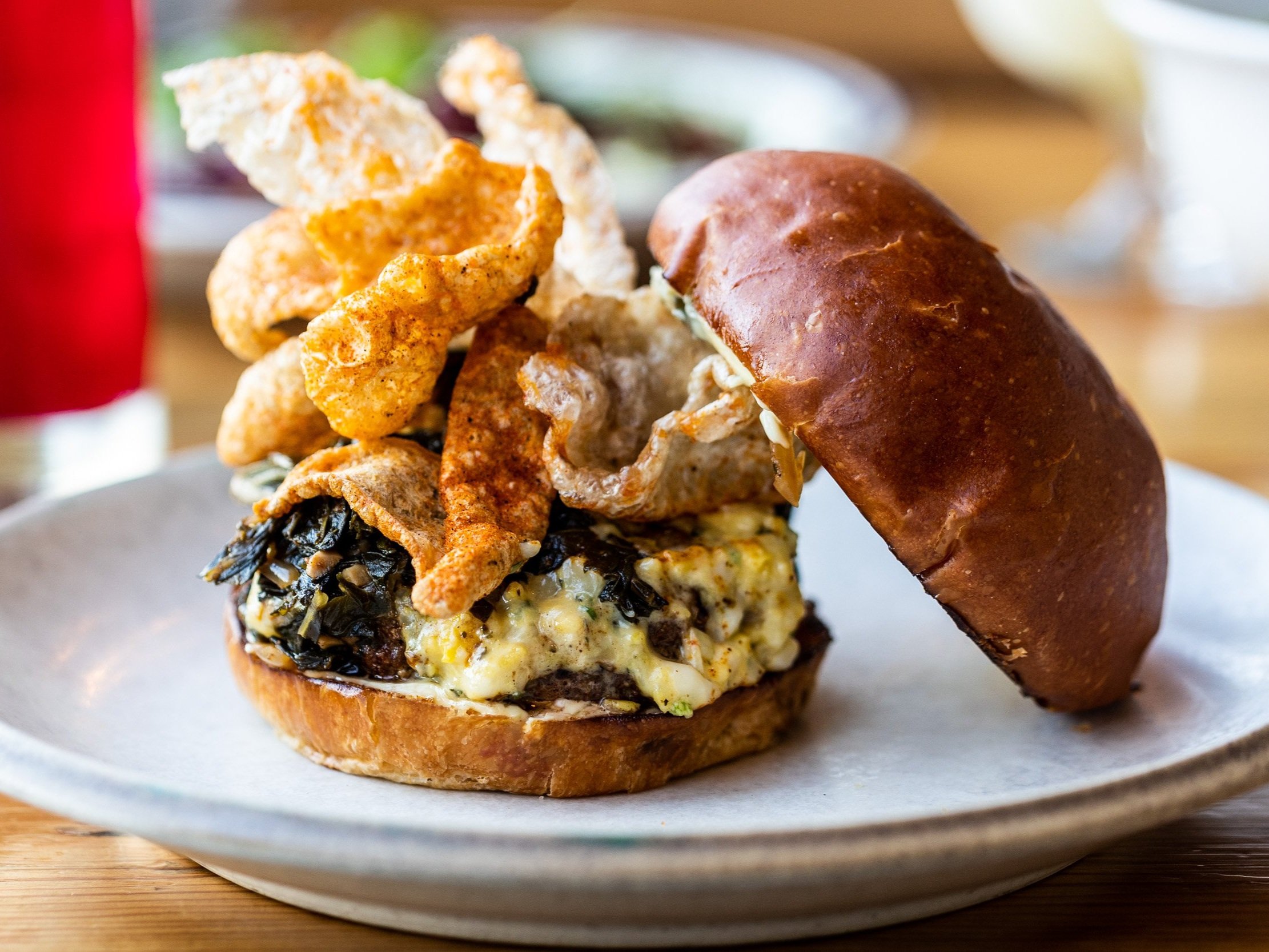 A burger with a meat patty, melty cheese, and crispy puffed chicharrones with the top slice off.
