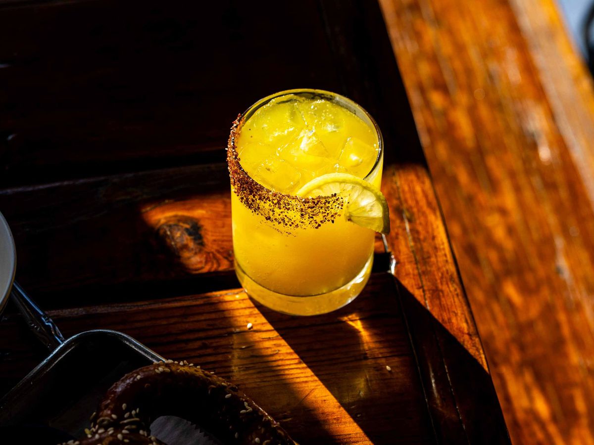 A yellow cocktail on a wooden table in sunlight.