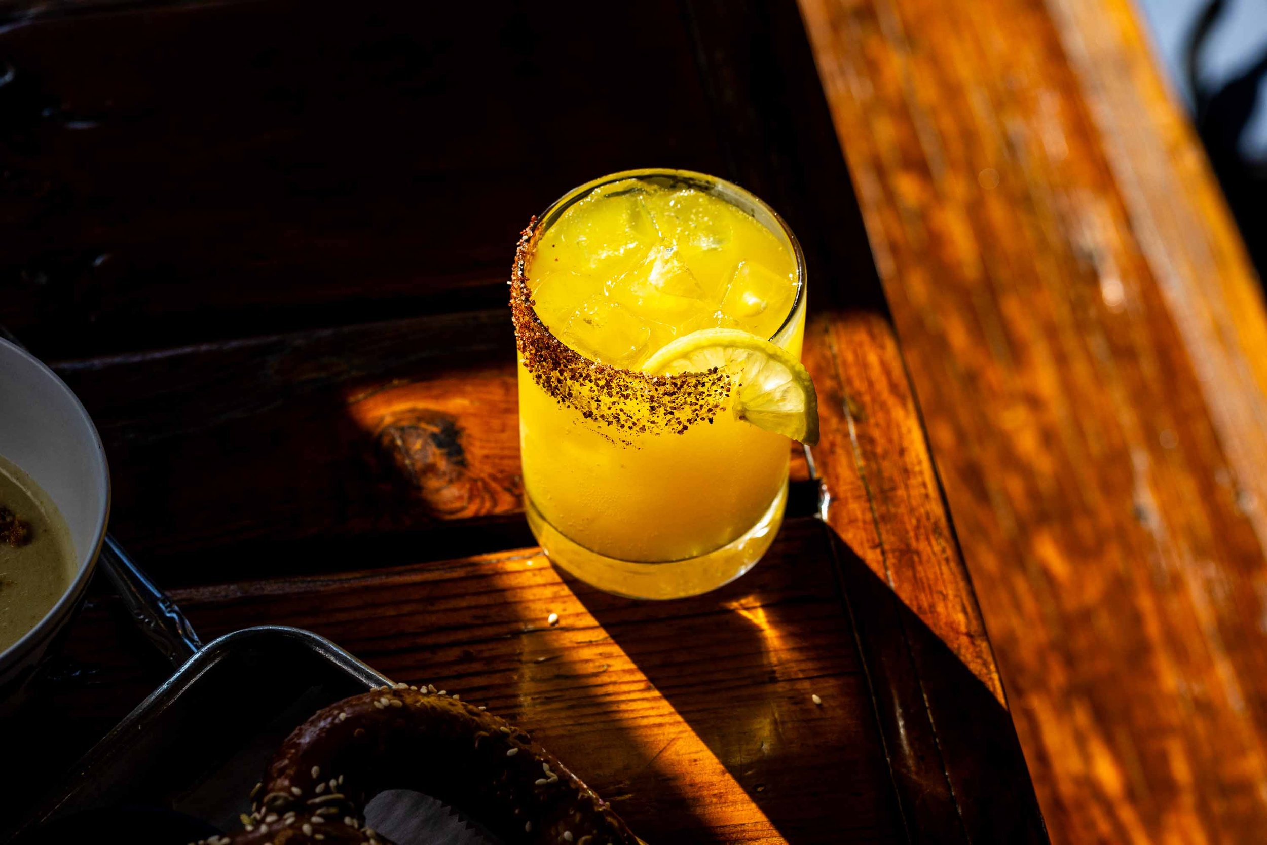 A yellow cocktail on a wooden table in sunlight.