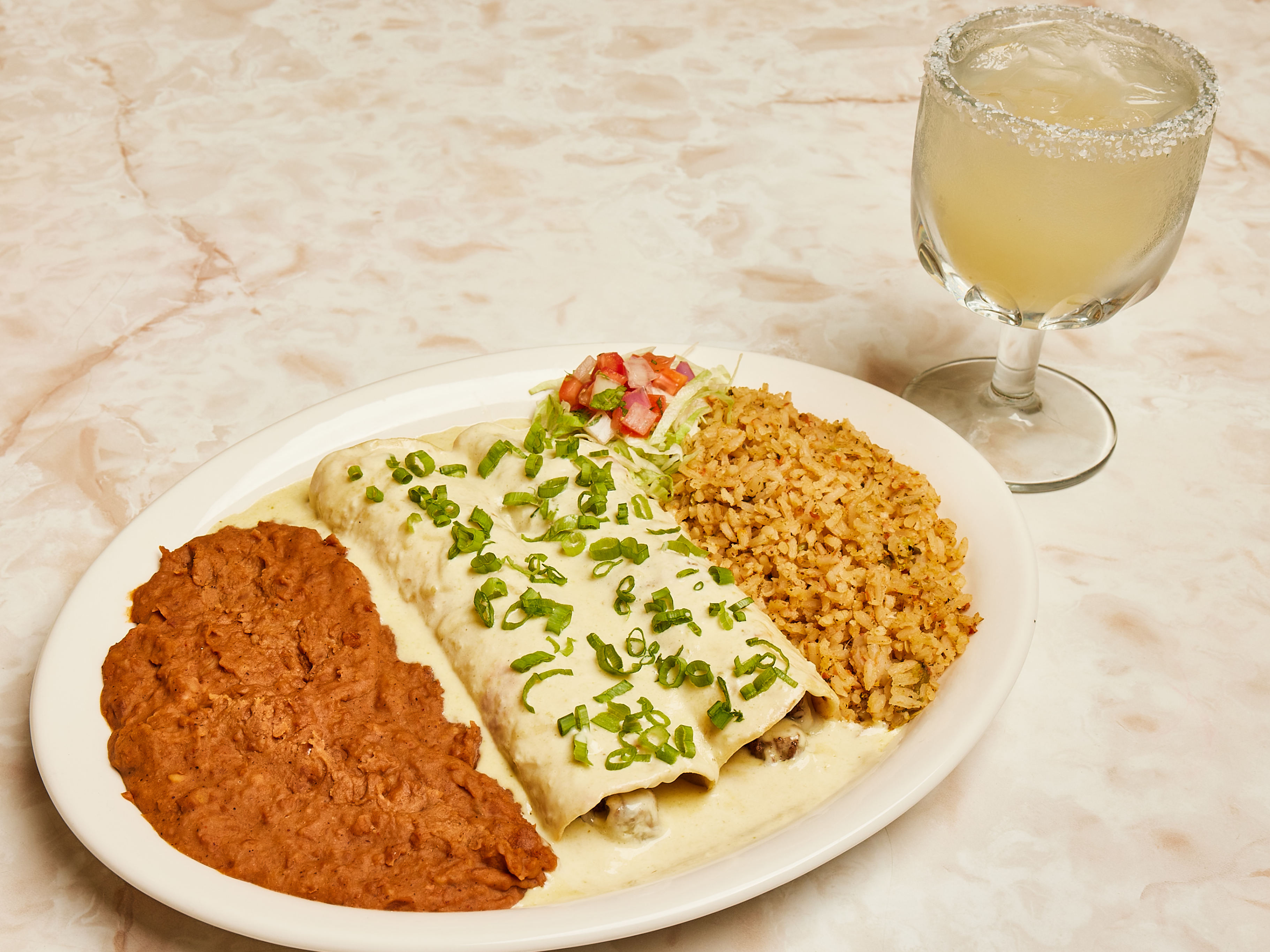 A plate holds sour cream enchiladas, rice, and refried beans.