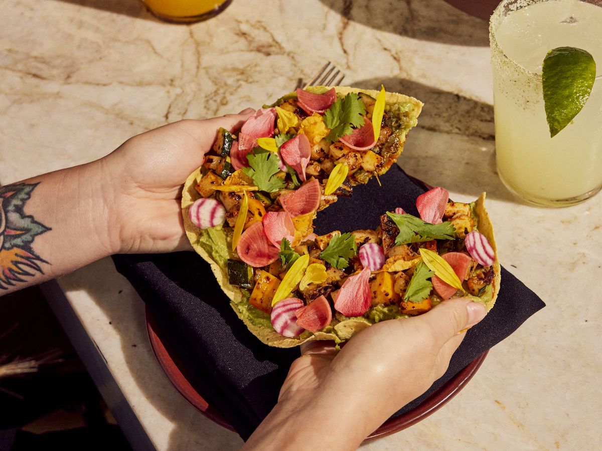 A pair of hands hold a vegan tostada with pickled radishes and fresh cilantro on top.