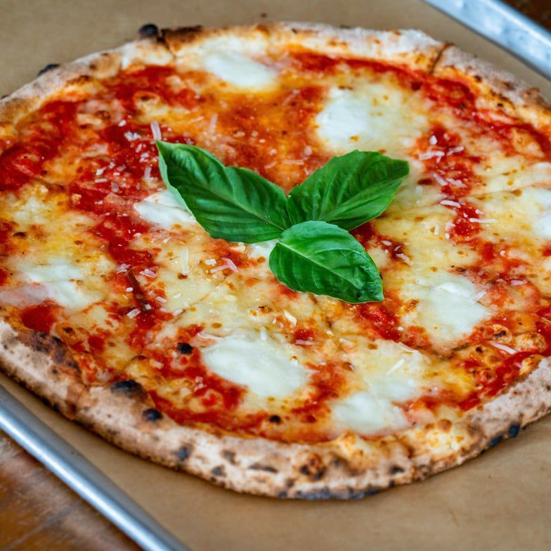 A margherita pizza topped with fresh basil sits on a silver tray.