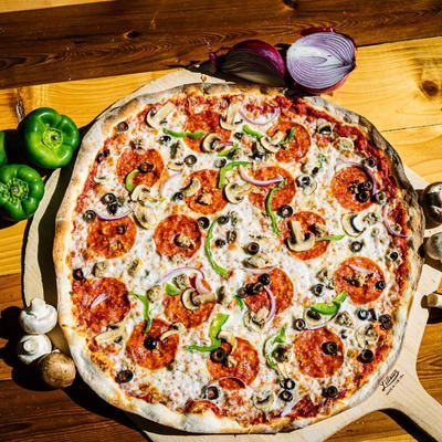 A large supreme pizza sits on a wooden board.