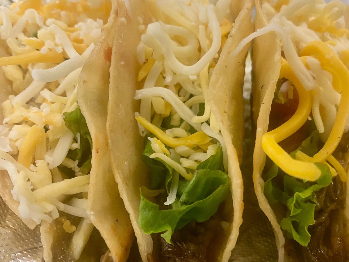 Three beef tacos with cheese and lettuce are crammed together.