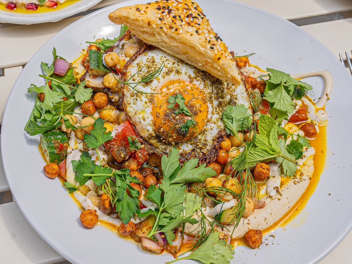 A white plate holds eggplant sabich with a slice of bread. 