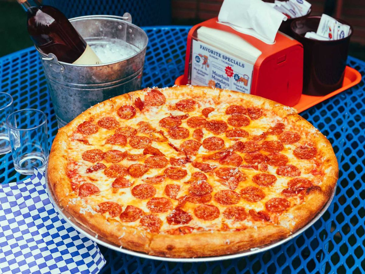 A pepperoni pizza sits on a stand atop a table with a blue and white checked table cloth.