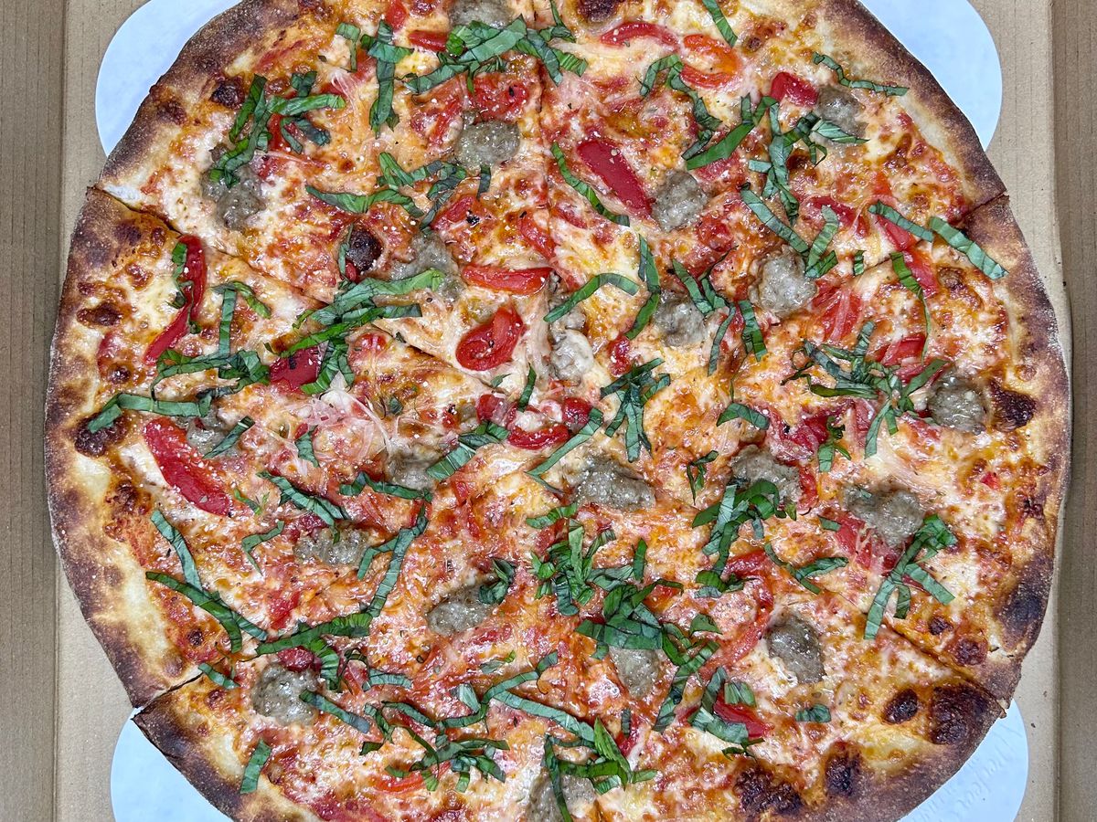 A pizza loaded with sausage, bell pepper, and onion sits in a delivery box.