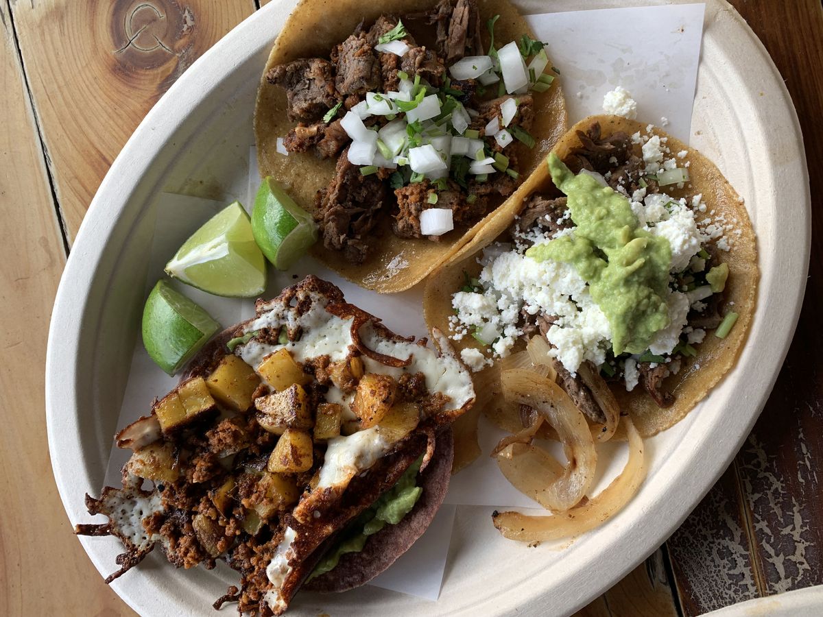A white plate of tacos with meats and vegetables.