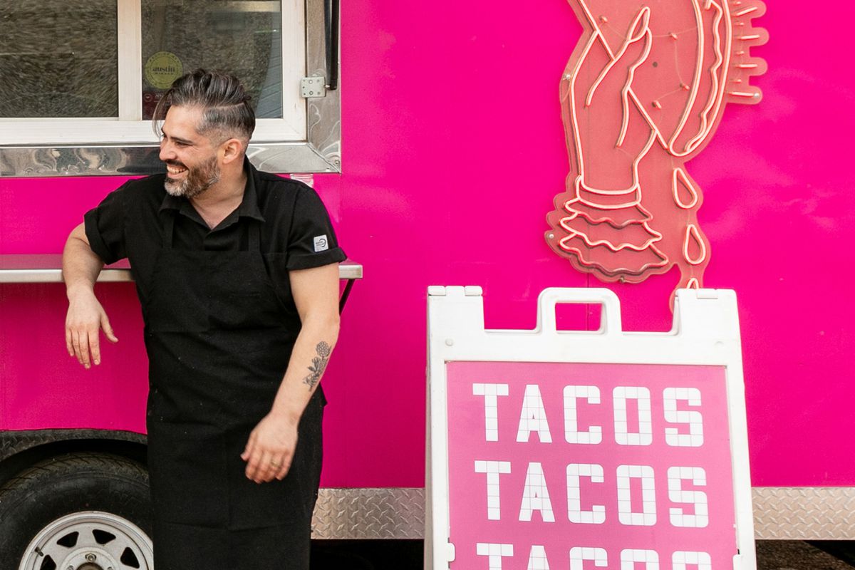 A man in black standing in front of a pink food truck.