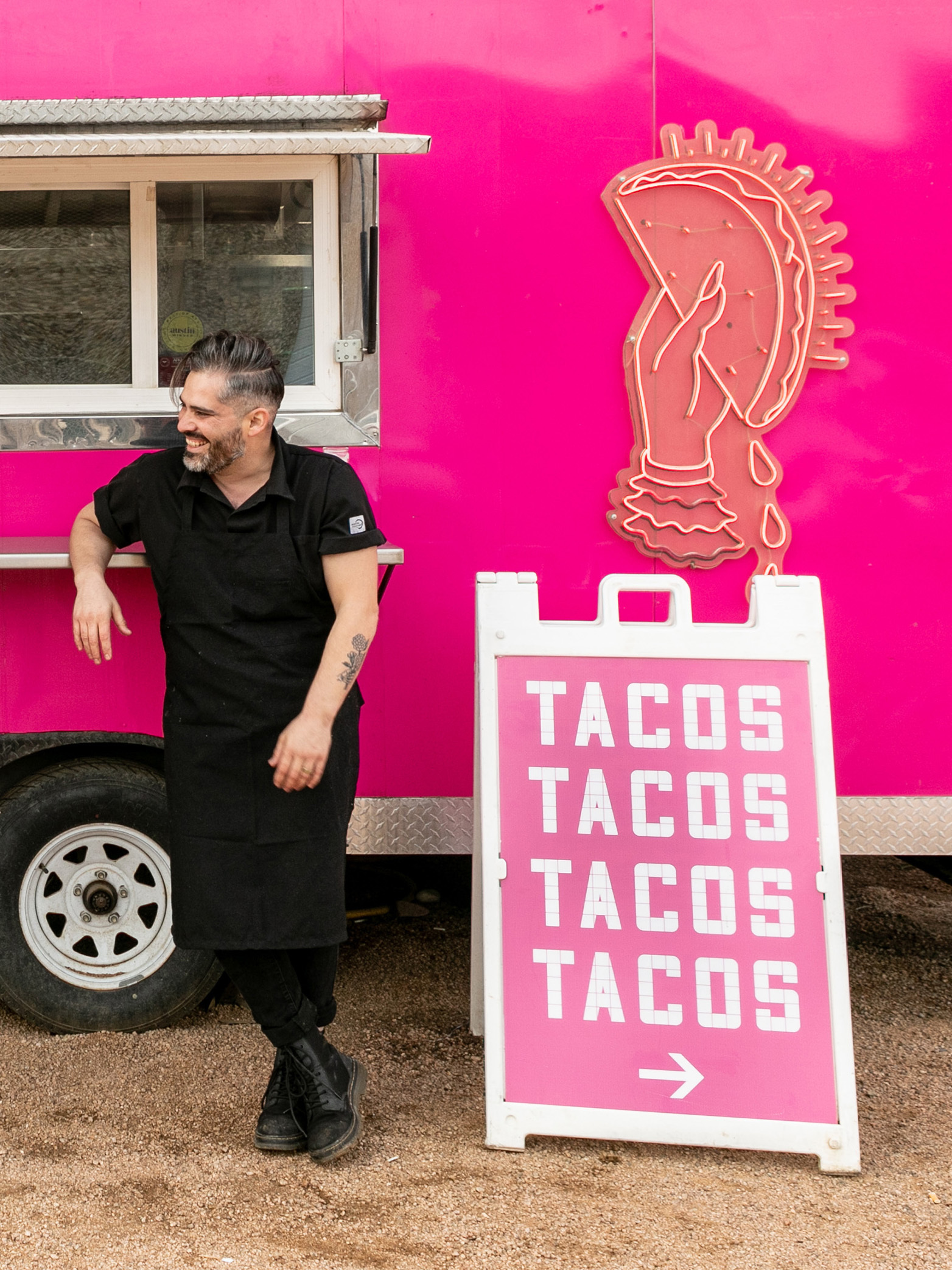A man in black standing in front of a pink food truck.