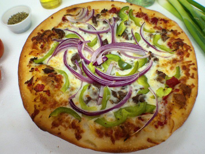 A pizza topped with red onions, bell peppers, and meat sits on a table.
