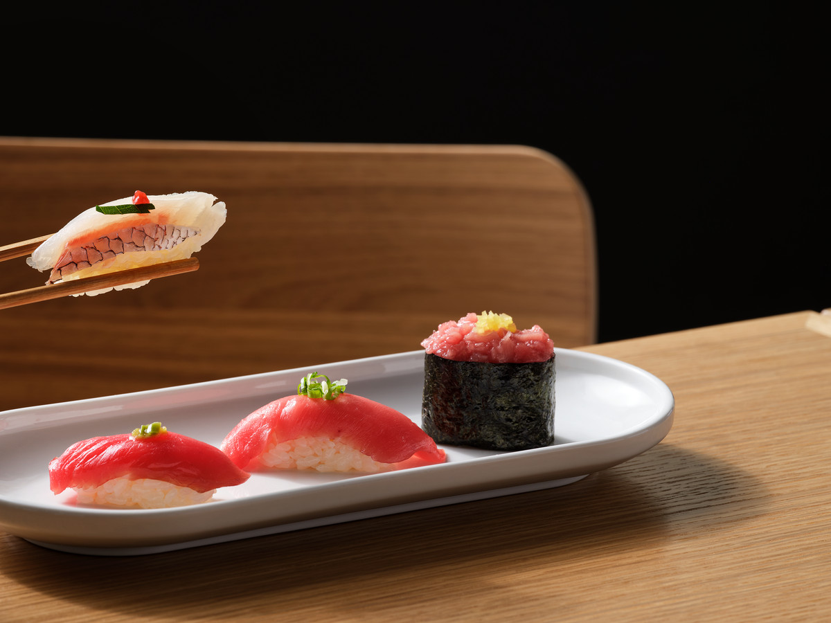 Someone picking up a sushi piece with chopsticks from a small place of three sushi.