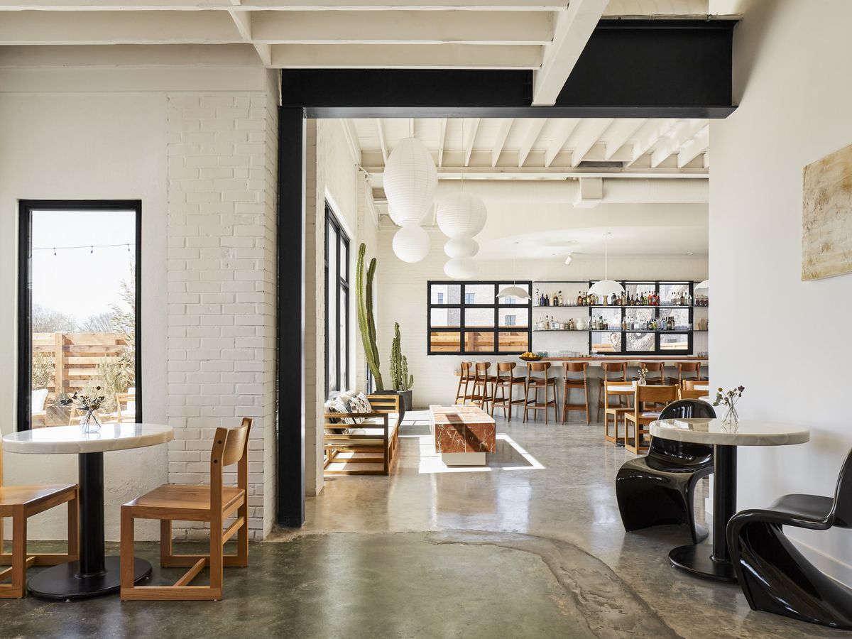 A light and airy bar with white walls has black and light wood furniture and cement floors.