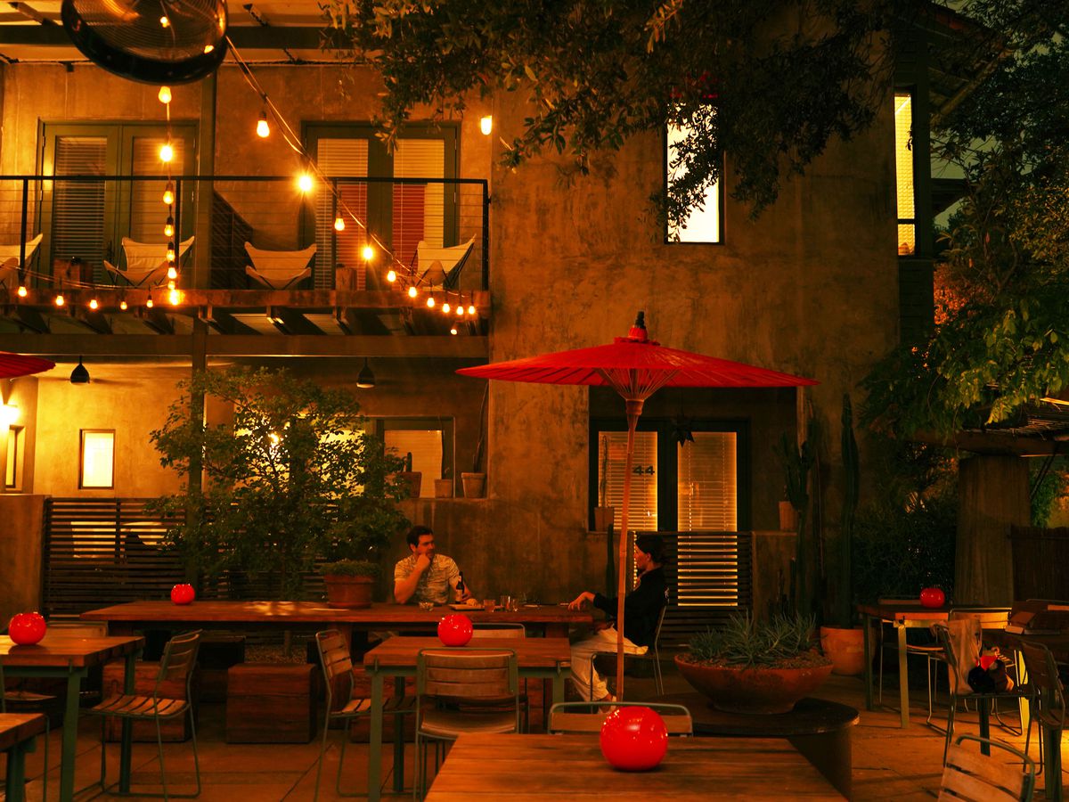 An outdoor bar is lit with twinkle lights. Red candles sit on wooden tables and one table has a red umbrella over it.