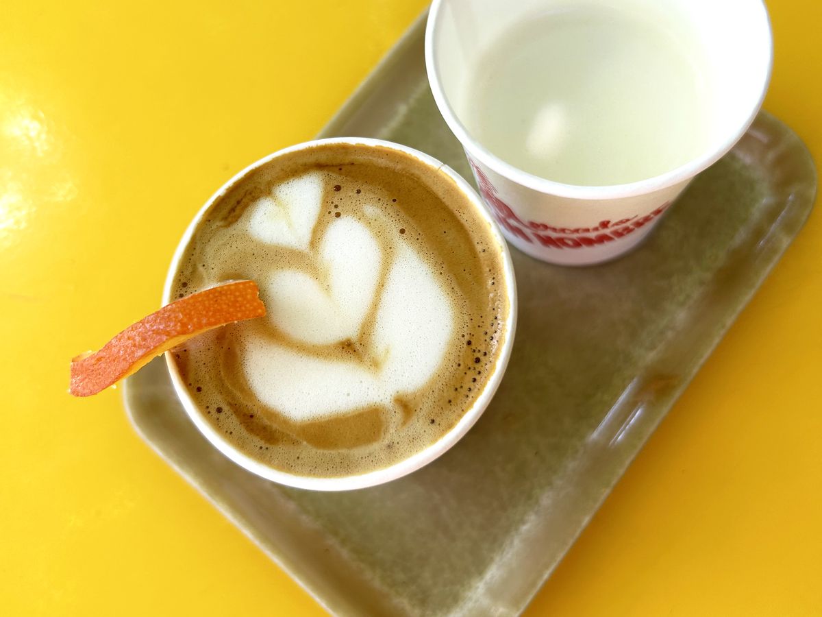 A birds-eye view of a cup of coffee with an orange slice and another cup of milk.