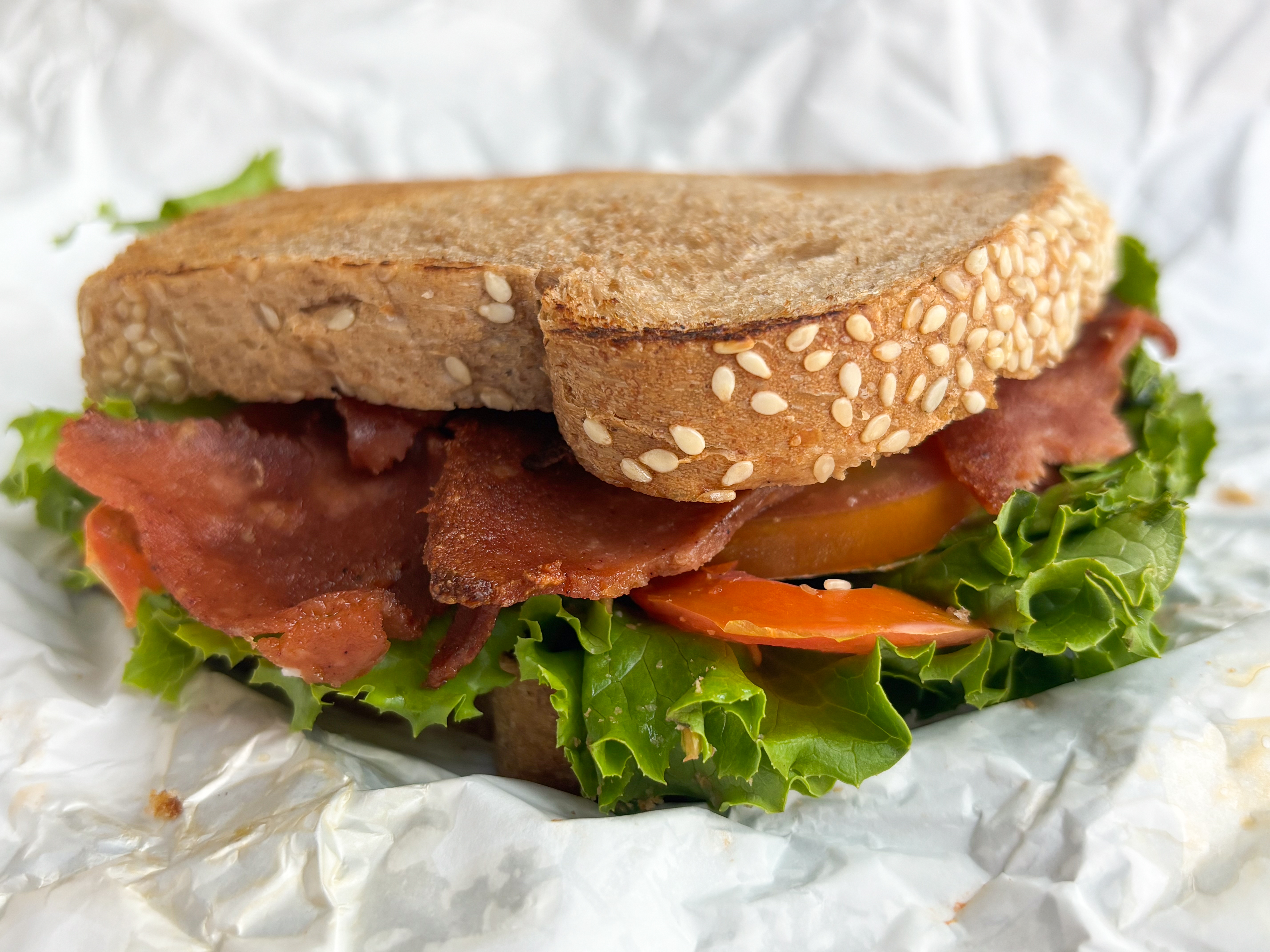 A BLT is served in a sandwich with lettuce and bacon coming out of the sides. The sandwich sits on a piece of crumpled wrapper paper.
