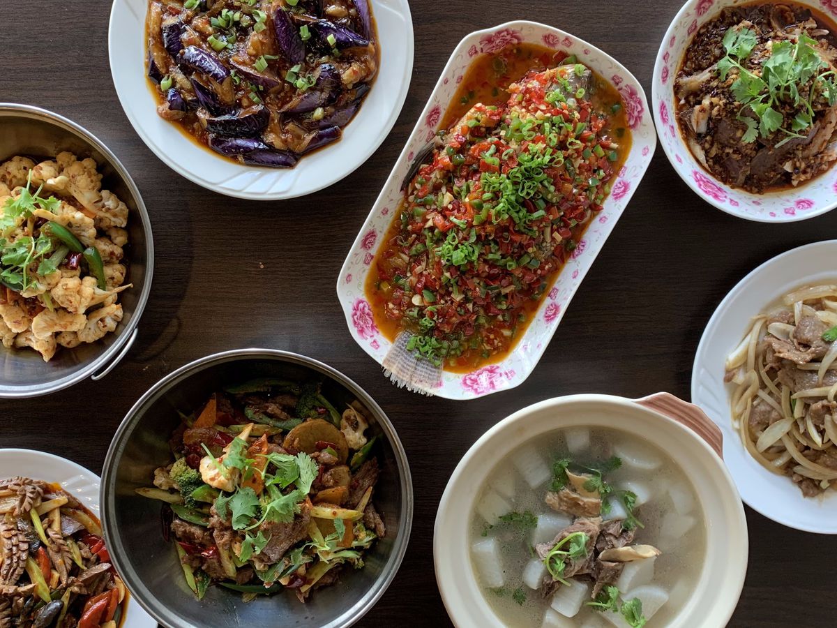 A variety of Sichuan dishes from House of Three Gorges including soup, noodles, and vegetables arranged on a dark wooden tabletop.