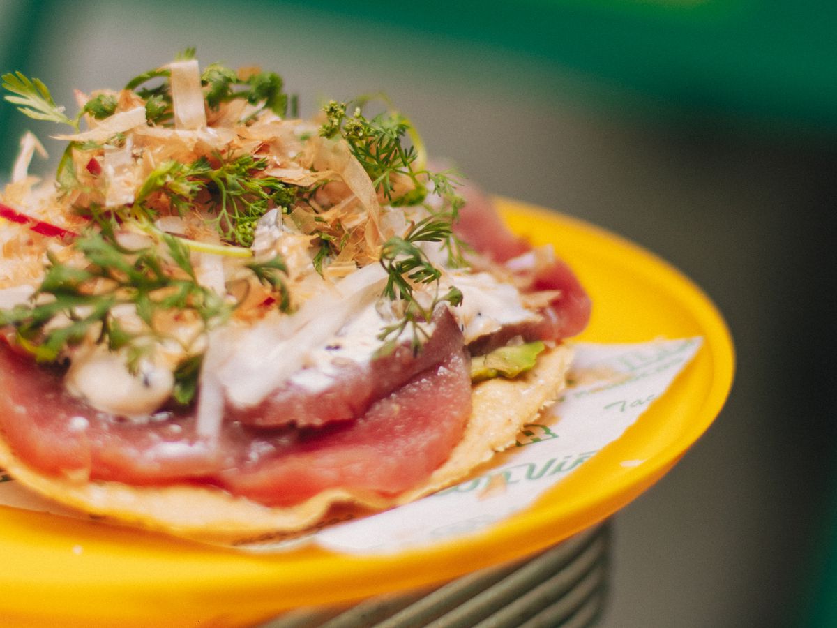A plate of a crispy tortilla topped with sliced fish and vegetables and condiments.