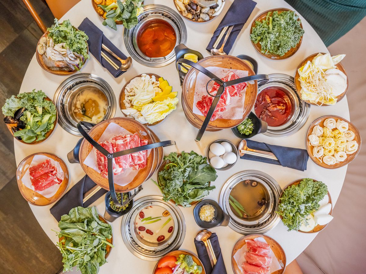 A round table full of plates of food and hot pots.