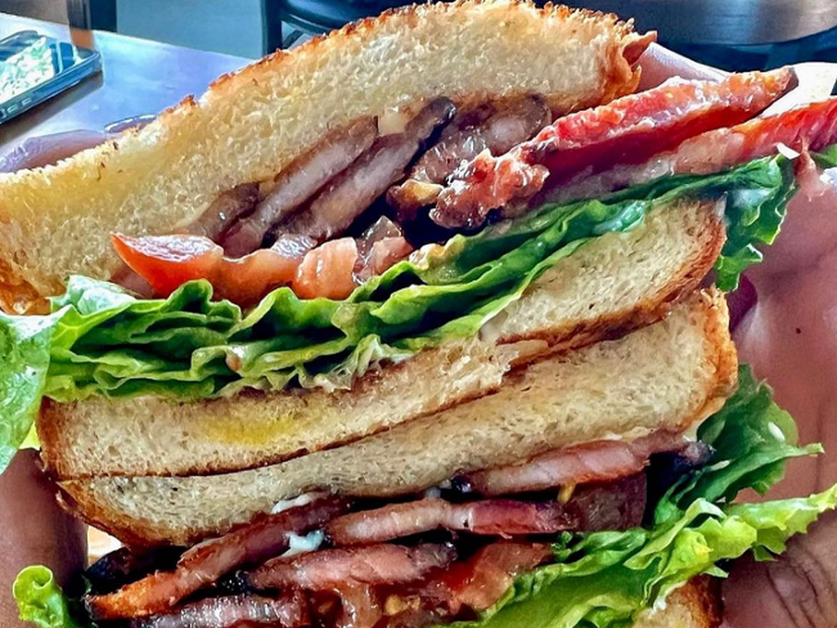 Someone holding up a halved sandwich with lettuce, bacon, and tomatoes.