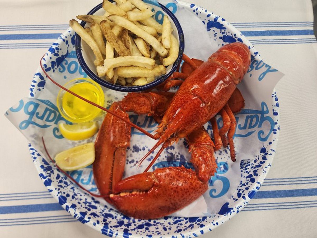A plate of a lobster with lemon wedges and fries.
