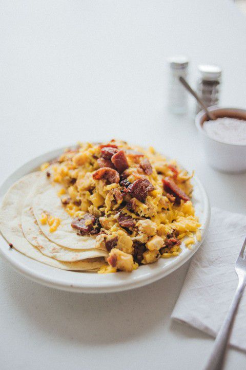 A breakfast taco sits on a plate. It’s loaded with scrambled eggs and bacon.