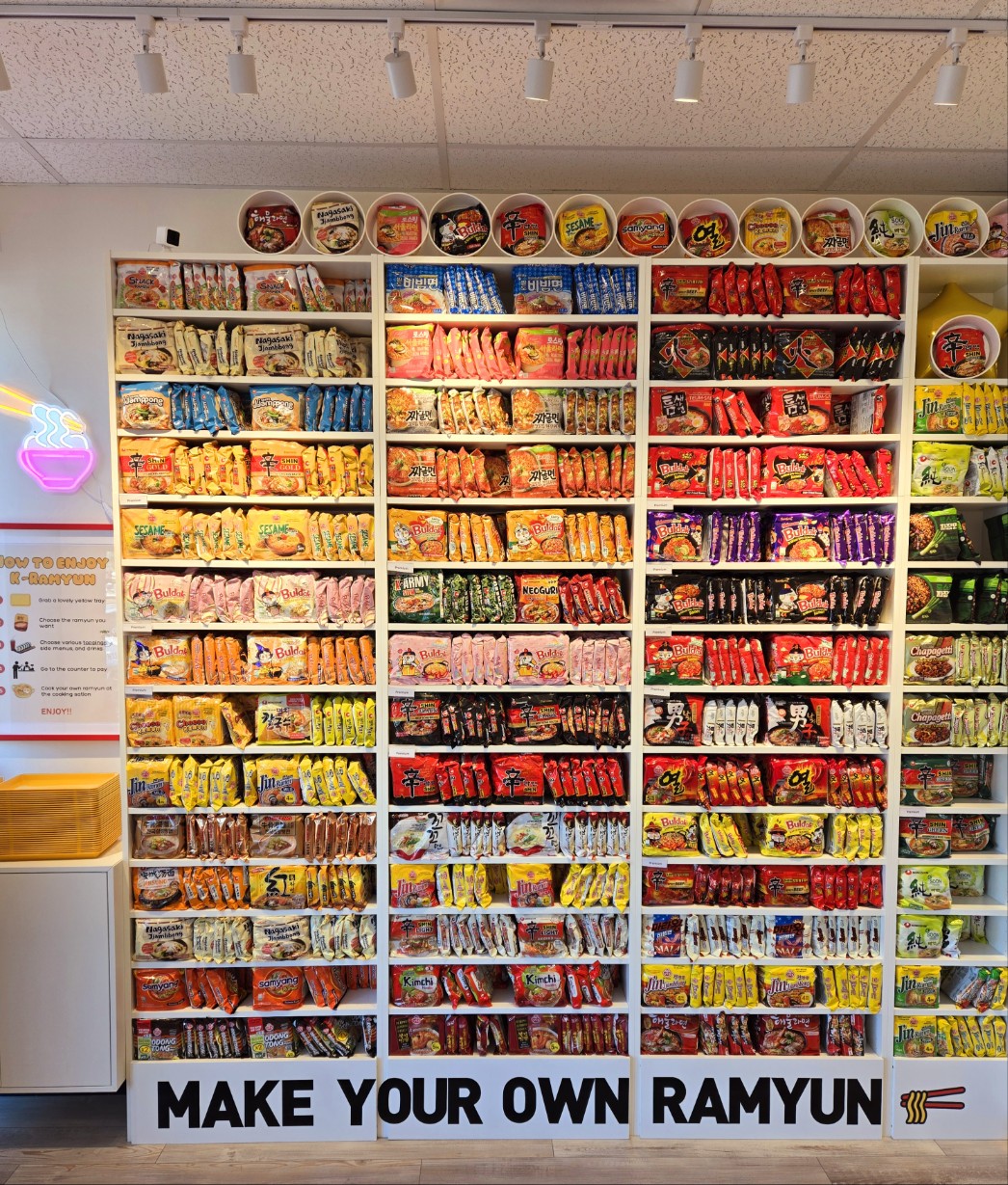 Shelves with packaged ramen and words on the bottom reading “Make Your Own Ramyun.”
