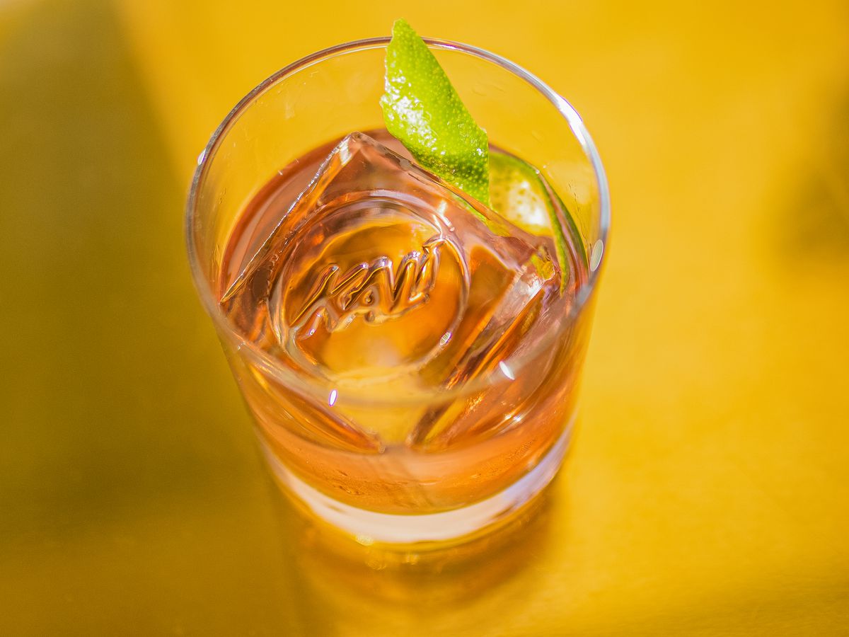 A golden-orange cocktail in a short glass with an ice cube.