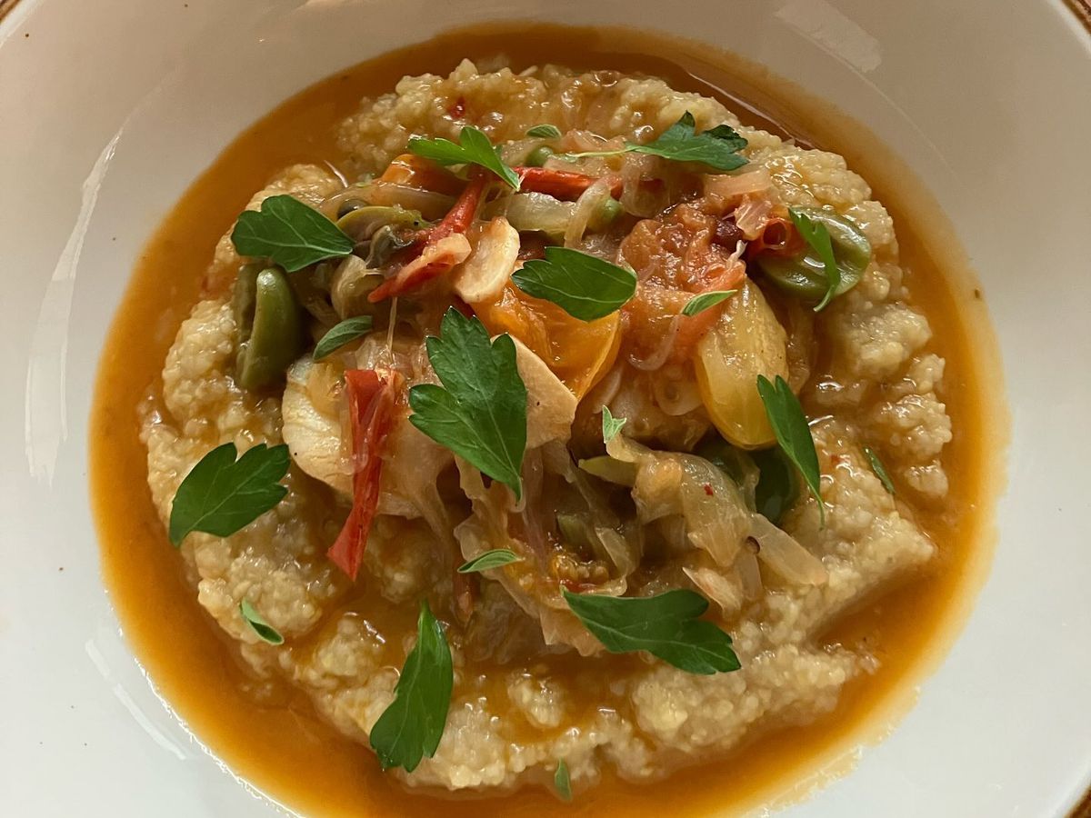 A bowl of polenta with consomme and fresh herbs. 