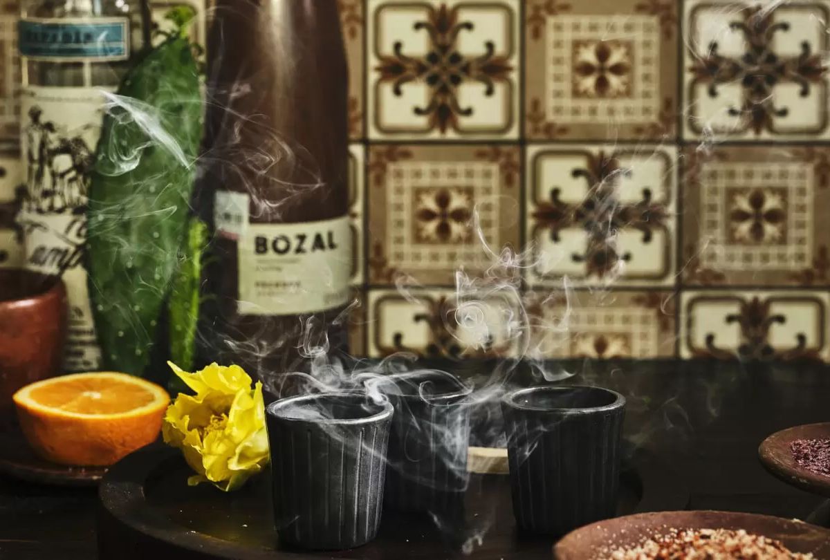 Three steaming glasses with cocktails sit on a table. Behind is a bottle of wine.